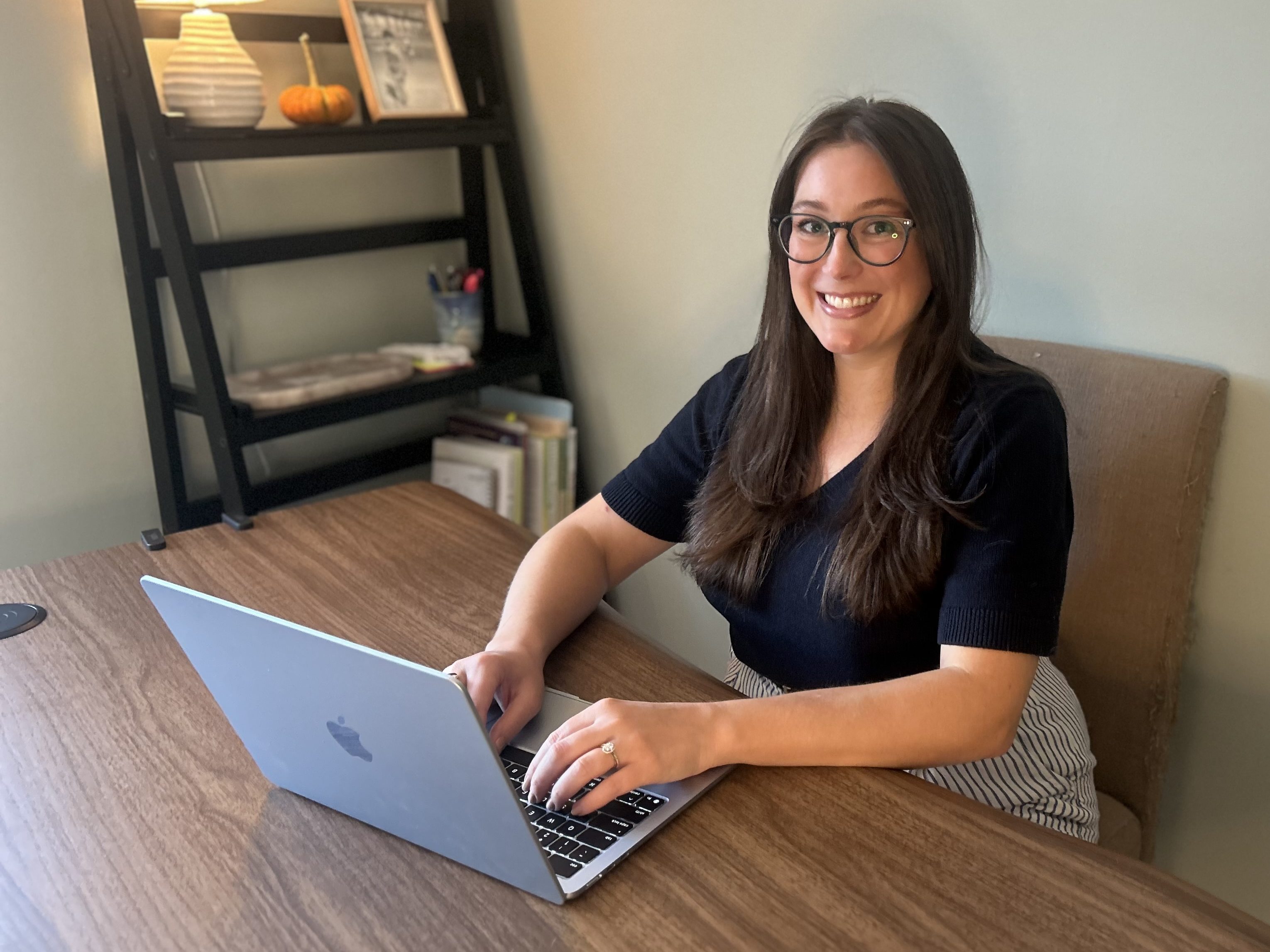 business owner at desk working on laptop, smiling at camera